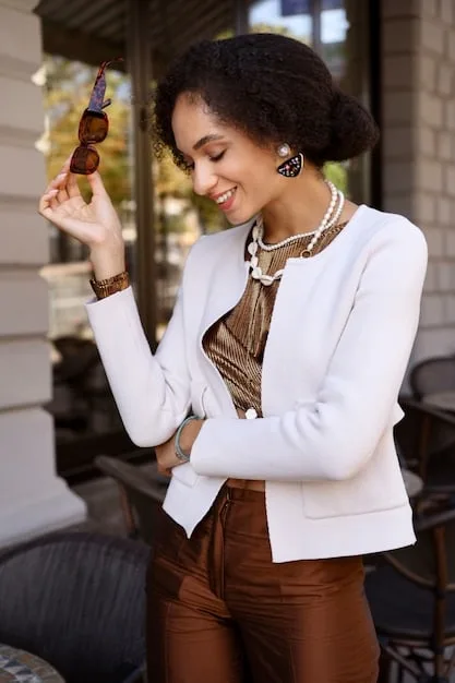 A woman wearing a Shein blazer, accessorized with a thin gold chain necklace and a statement geometric ring. She is in a modern office environment, smiling confidently.