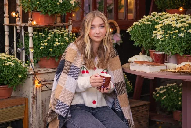 A woman in an oversized knit sweater and distressed denim shorts, sitting at an outdoor cafe with a coffee, showcasing the weekend chic outfit. She is smiling and has a relaxed, carefree vibe.