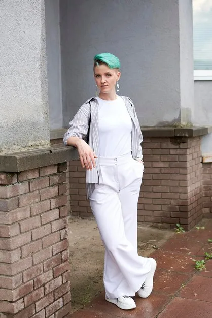 A woman is standing in front of a brick wall, wearing wide-leg khaki trousers, a red and white striped knit sweater, and white sneakers. She is holding a small leather bag and smiling confidently. The image highlights the balance between comfort and style in the outfit.