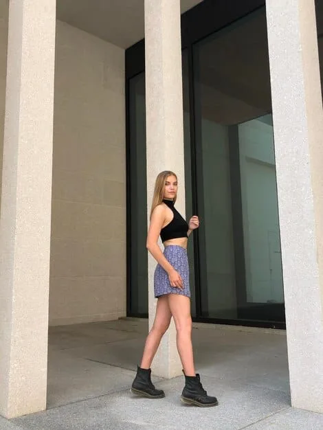 A woman with an inverted triangle body shape walking down a street, wearing a simple V-neck top with wide-leg trousers and sneakers. The wide-leg trousers add volume to her lower body, creating a balanced silhouette.