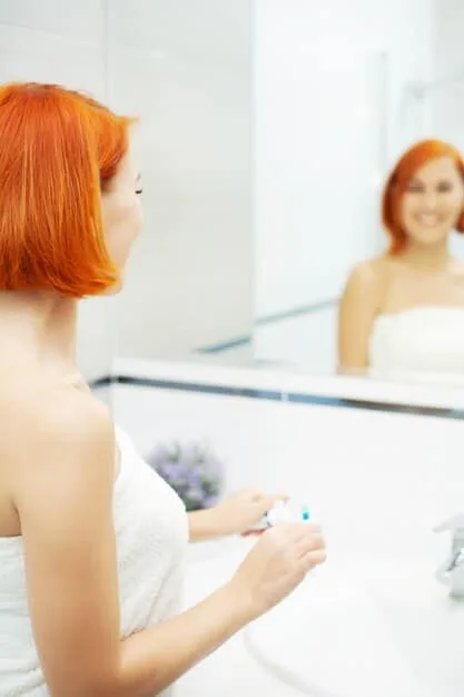 A woman applying hydrating serum to her face. The background is a bright, modern bathroom.