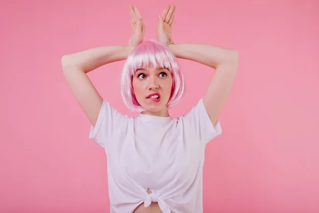 A woman with short, pastel pink hair. The hair is styled in a sleek bob, and she is wearing a white t-shirt. The background is a soft, pastel-colored wall.
