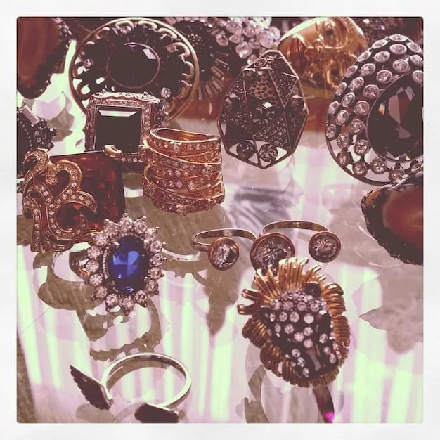 A photograph showcasing an assortment of statement rings with chunky designs and gem embellishments, displayed neatly on a velvet tray. The rings feature various metals like gold and silver, and are styled for a modern luxury look.