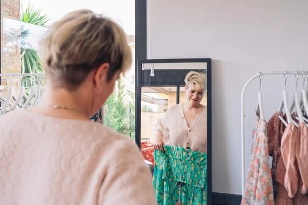 A woman standing in front of a large mirror, trying on different outfit combinations from her capsule wardrobe. The wardrobe consists of classic, versatile pieces in neutral colors like black, white, and gray. She is smiling and appears confident and stylish.