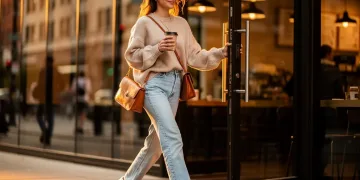Stylish woman in a casual coffee-run ensemble, holding a cup, walking from a cafe.