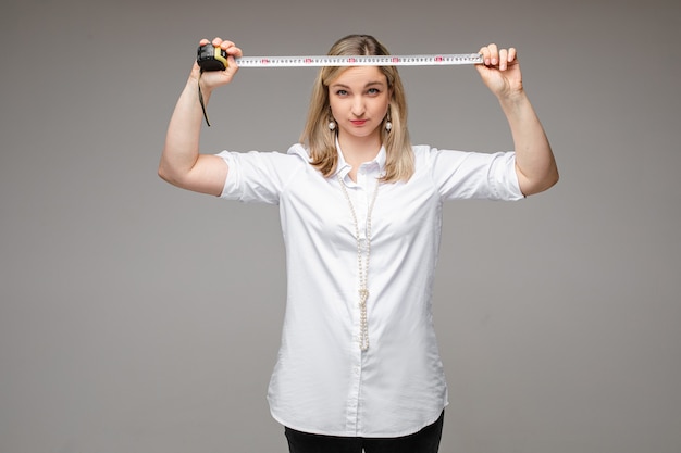 A woman using a measuring tape to measure her waist, with a focus on the correct placement of the tape and posture.