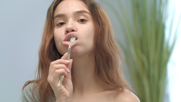 A woman gently exfoliating her lips with a soft toothbrush, followed by the application of a clear lip balm. The focus is on the gentle circular motions of the toothbrush and the smooth texture of the balm.