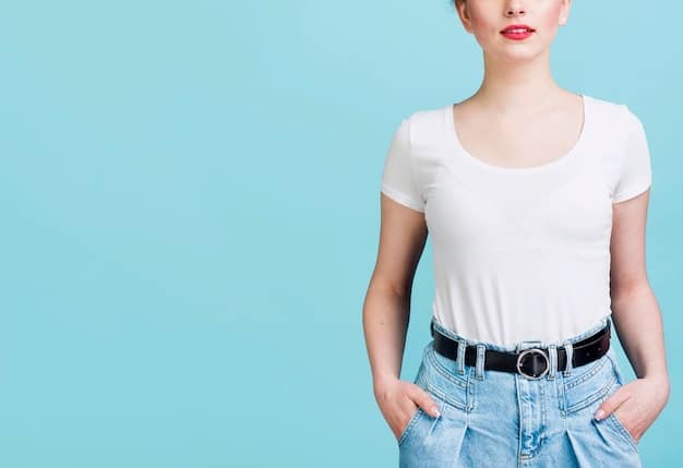 A close-up shot of a woman wearing a white t-shirt tucked into high-waisted light wash jeans, accessorized with a brown leather belt and delicate gold jewelry. The focus is on the texture of the denim and the clean lines of the overall outfit.