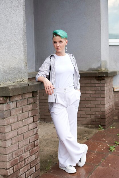 A woman is standing in front of a brick wall, wearing wide-leg khaki trousers, a red and white striped knit sweater, and white sneakers. She is holding a small leather bag and smiling confidently. The image highlights the balance between comfort and style in the outfit.