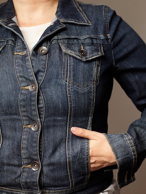 A close-up shot of a woman wearing a denim jacket over a striped Breton top, paired with dark wash jeans and brown leather boots. The focus is on the texture and layers of the outfit.