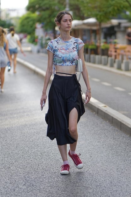 A full-length shot of a woman wearing a flowy tunic top in a floral print, paired with dark wash skinny jeans and ballet flats. She is holding a tote bag and walking down a city street.