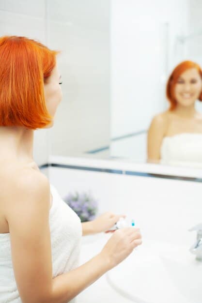 A woman applying hydrating serum to her face. The background is a bright, modern bathroom.