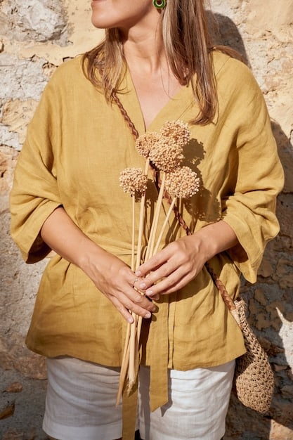 A model wearing a flowing terracotta-colored dress at NYFW 2024, exuding an earthy, bohemian vibe, complemented by minimalist jewelry and sandals, embodying the trend of natural, muted tones.