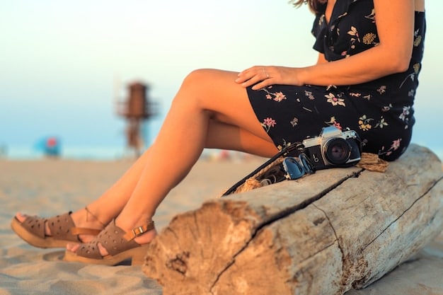 A closeup of a woman's legs, showcasing her tanned skin, a delicate anklet, and tan cowboy boots. She's standing on a sandy beach with the ocean blurred in the background.