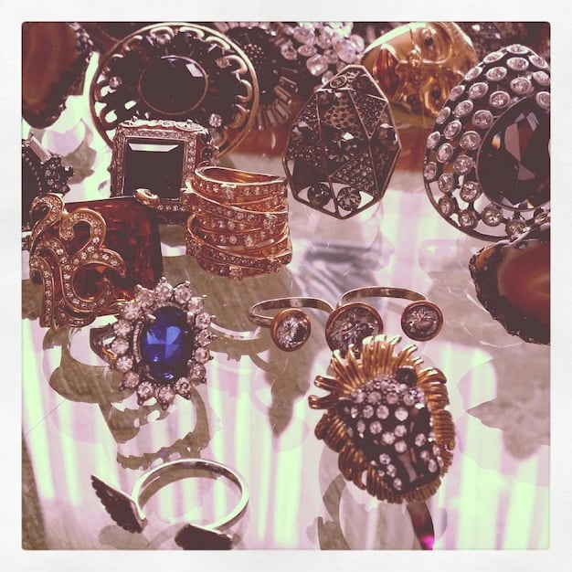 A photograph showcasing an assortment of statement rings with chunky designs and gem embellishments, displayed neatly on a velvet tray. The rings feature various metals like gold and silver, and are styled for a modern luxury look.