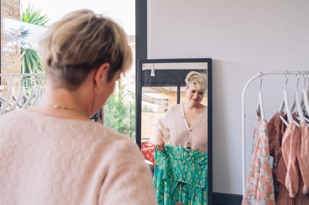 A woman standing in front of a large mirror, trying on different outfit combinations from her capsule wardrobe. The wardrobe consists of classic, versatile pieces in neutral colors like black, white, and gray. She is smiling and appears confident and stylish.