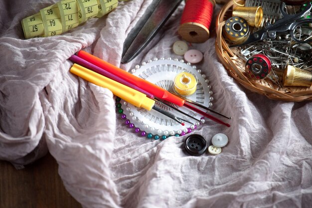 Close-up of a sewing kit with various items such as needles, threads of different colors, scissors, measuring tape and seam ripper, placed on top of a colorful fabric.