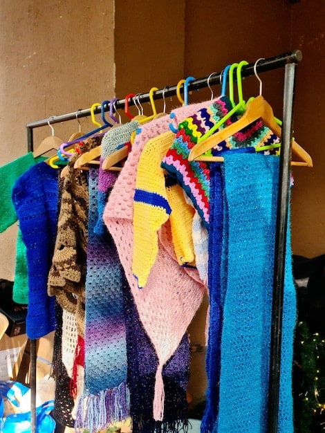 A close-up shot of a rack of colorful and diverse clothing items in a thrift store, with a focus on textures like lace, corduroy, and denim. The image captures the organized chaos of thrift store shopping, with various styles and patterns visible.