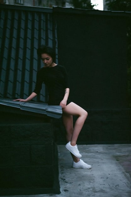 A woman wearing Shein's black slip dress, paired with minimal gold jewelry and white sneakers, in a minimalist, urban setting with soft, diffused lighting.