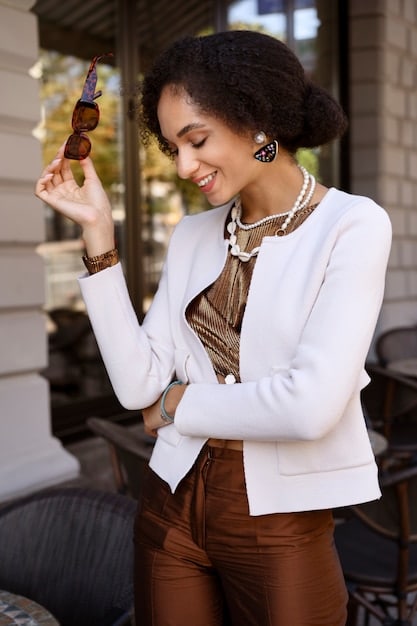 A woman wearing a Shein blazer, accessorized with a thin gold chain necklace and a statement geometric ring. She is in a modern office environment, smiling confidently.