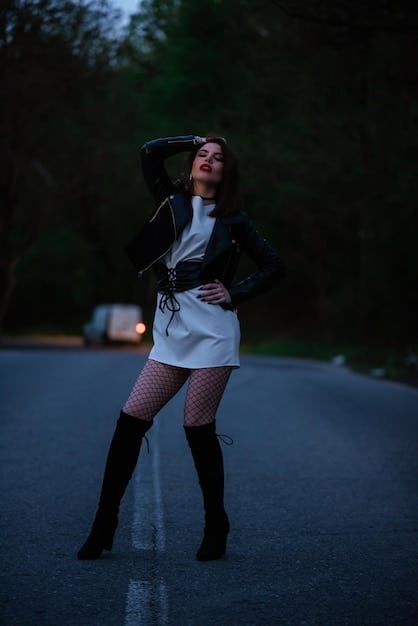 A woman standing confidently in a dimly lit club, wearing a leather skirt, a band tee, and strappy heels, showcasing a powerful and edgy night-out ensemble. The lighting highlights the textures and details of the outfit.