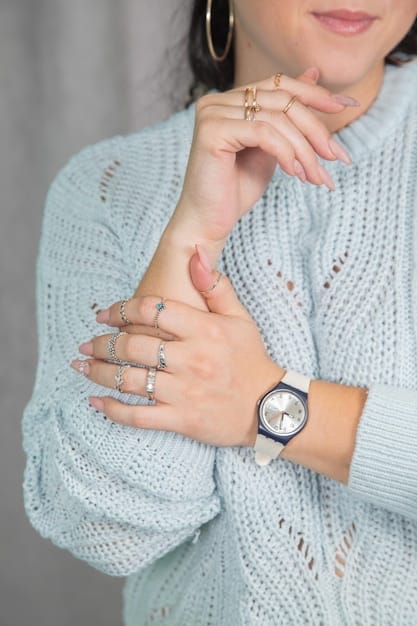 A close-up of a stylish woman's wrist adorned with a simple silver watch and a delicate bracelet, next to a stack of well-organized, neutral-colored clothing, symbolizing thoughtful accessorizing within a minimalist wardrobe.