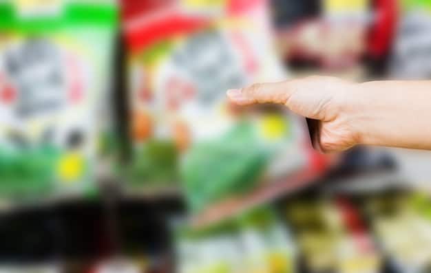 A close-up of a hand inspecting a product label featuring various eco-friendly certifications and symbols, with a blurred background of supermarket shelves, symbolizing informed consumer choices.