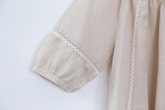 A close-up of a blouse sleeve featuring intricate smocking details on pastel-colored linen, showing the textured fabric and precise stitching.