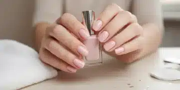 Hands with perfectly polished light pink nails, holding a nail polish bottle, demonstrating a successful at-home manicure.